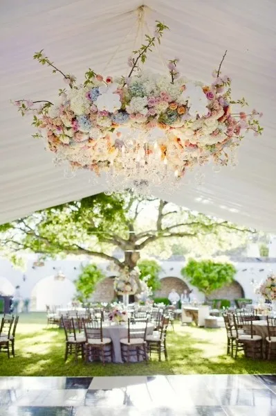 A floral chandelier hanging in a marquee, looking out to a garden