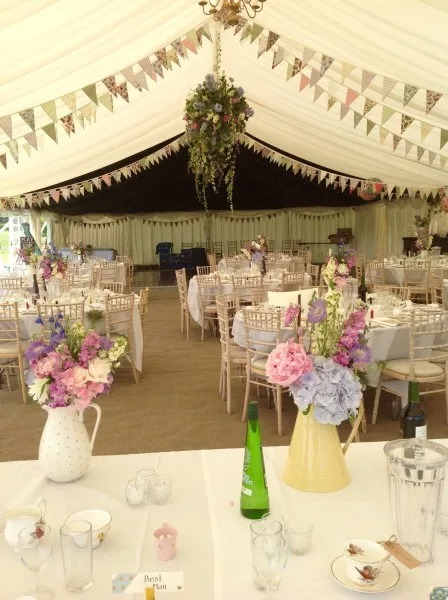 Jugs of country flowers on tables in a marquee hung with bunting