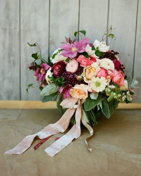 A hand-tied bouquet in pinks and plums with trailing ribbons