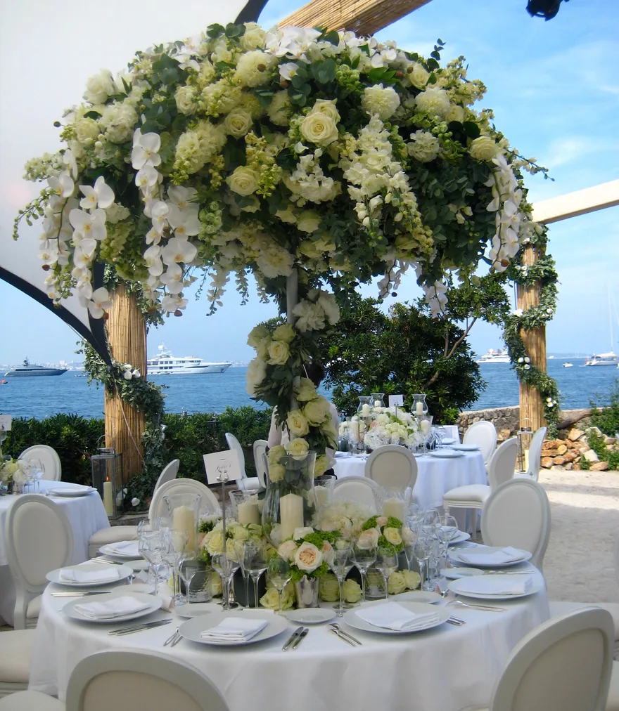 A towering white floral centrepiece on a wedding table by the sea