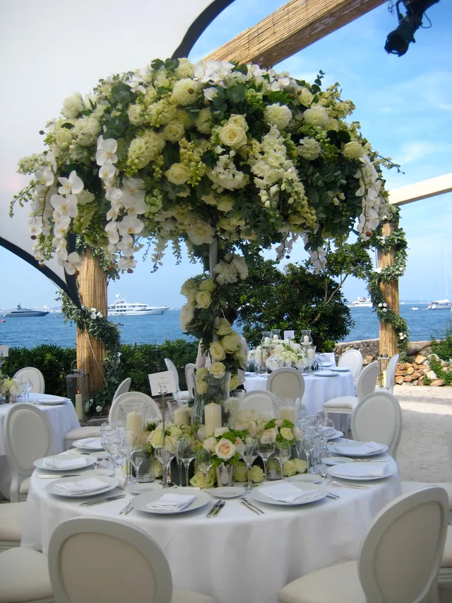 A towering white floral centrepiece on a wedding table by the sea