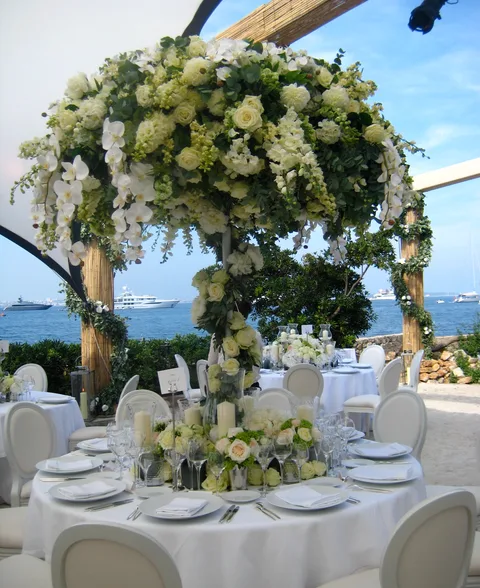 A towering white floral centrepiece on a wedding table by the sea